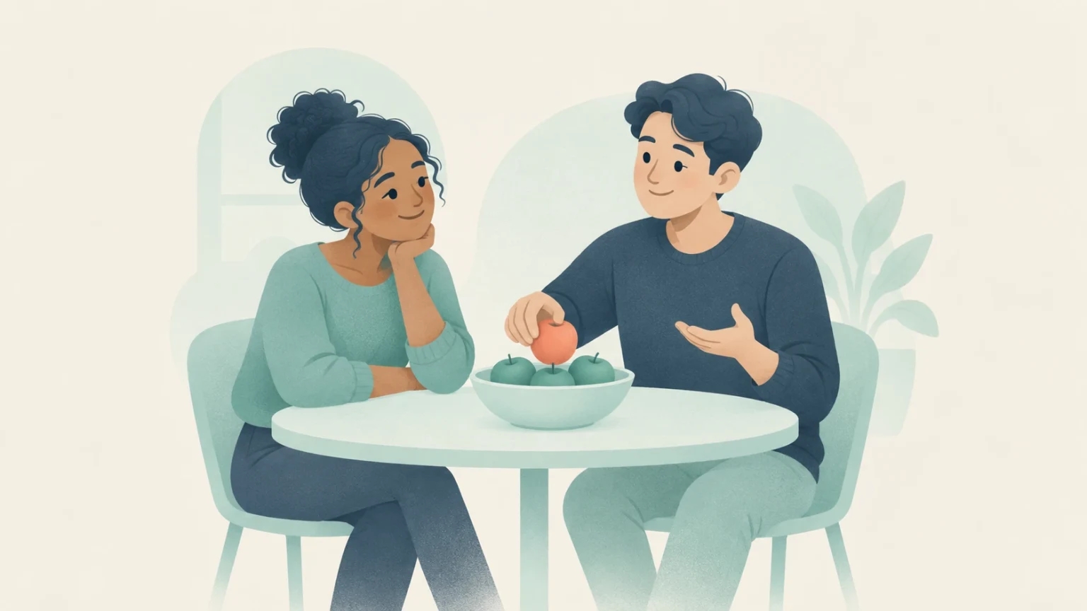 Two people converse at a round table with a bowl of apples; one holds a red apple and gestures while the other listens attentively.